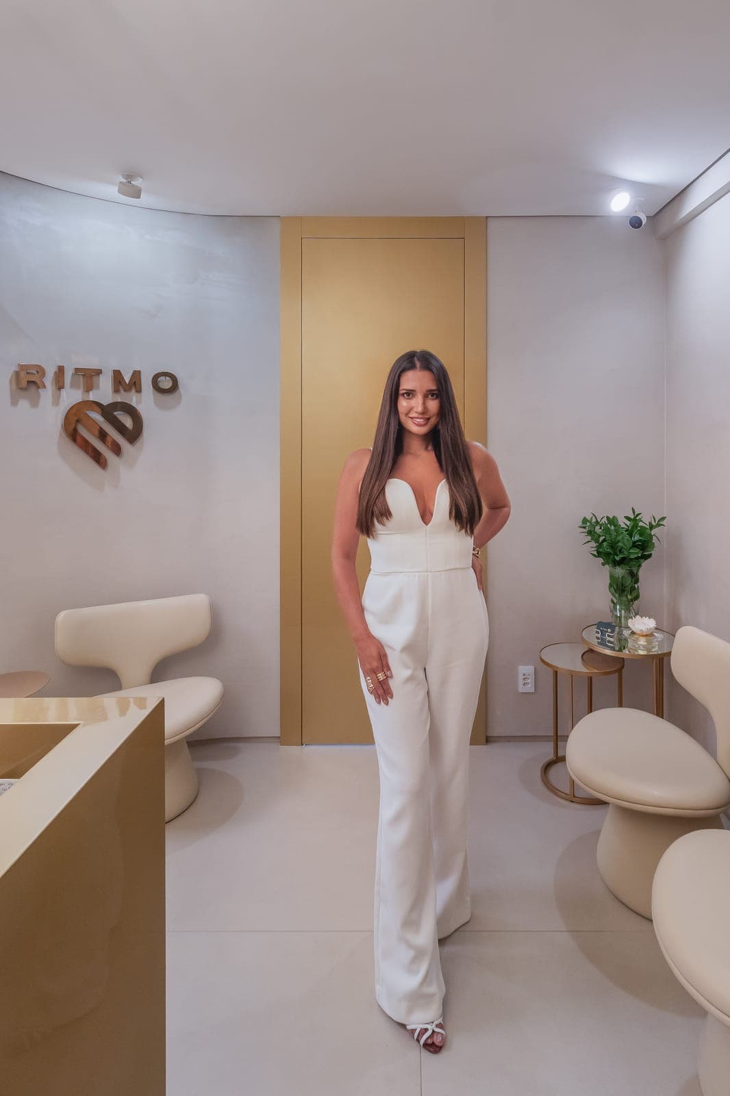 The architect in the reception of Clínica Ritmo, a project of hers, between cream armchairs and a gold door